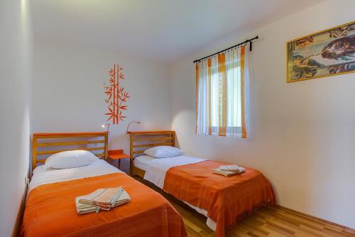 a bedroom with two beds with orange sheets and a window at Apartman Astrid in Veli Lošinj