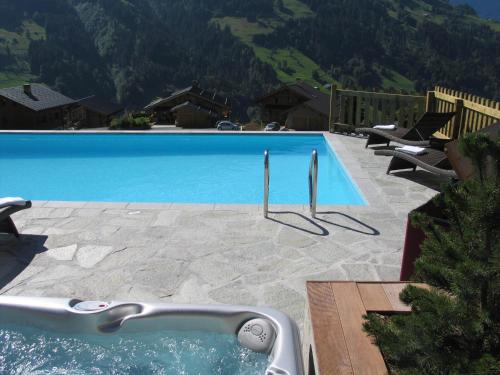a large blue swimming pool with mountains in the background at Hôtel La Ferme du Chozal, Chalet de tradition in Hauteluce