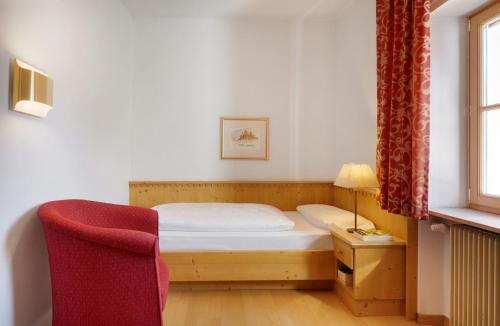 a small bedroom with a bed and a red chair at Parkhotel Post in Chiusa