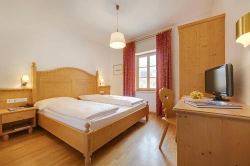 a bedroom with a bed and a desk with a tv at Parkhotel Post in Chiusa