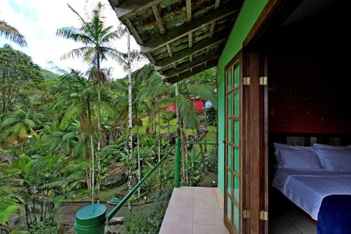 a room with a bed and a balcony with trees at Chalés Terras Altas de Paraty in Paraty