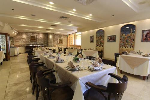 a row of tables in a restaurant with white table settings at Ambassador Hotel in Jerusalem