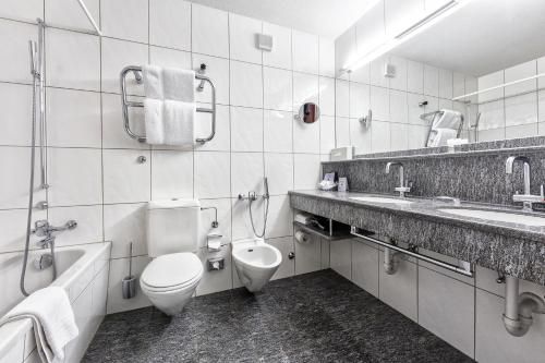 a bathroom with a toilet and a sink and a tub at Golf- & Sporthotel Hof Maran in Arosa