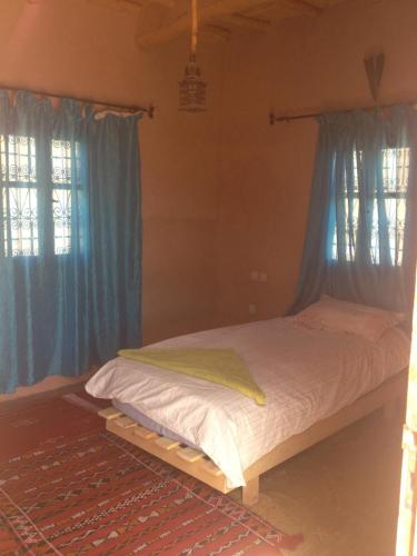 a bed in a bedroom with blue curtains at Kasbah Ounila in Aït Ben Haddou