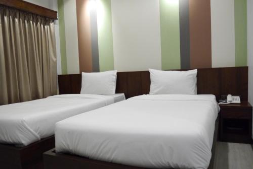 two beds in a hotel room with white sheets at Lertnimit Hotel in Chaiyaphum