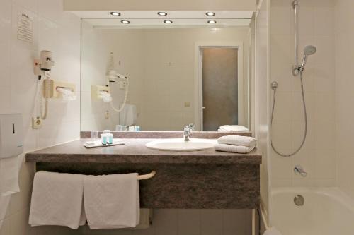 a bathroom with a sink, mirror, towel rack and towel dispenser at Hotel Figaro in Knokke-Heist