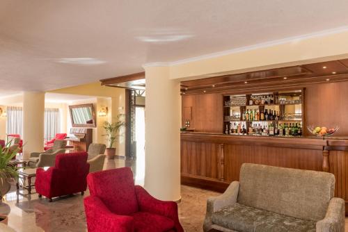 un vestíbulo con un bar con sillas rojas en Sunset Hotel, en Corfú