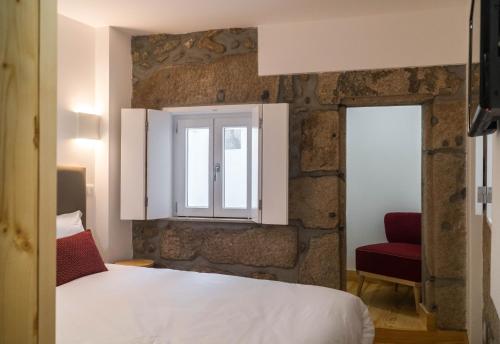 a bedroom with a bed and a window and a red chair at Ribeiredge Guest House in Porto