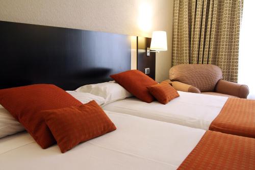 a hotel room with two beds and a chair at Hotel Conde Duque Bilbao in Bilbao