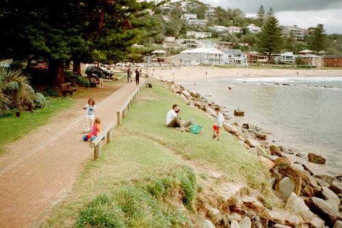 a group of people sitting on a bench next to a beach at Avoca Beach and Bush in Avoca Beach