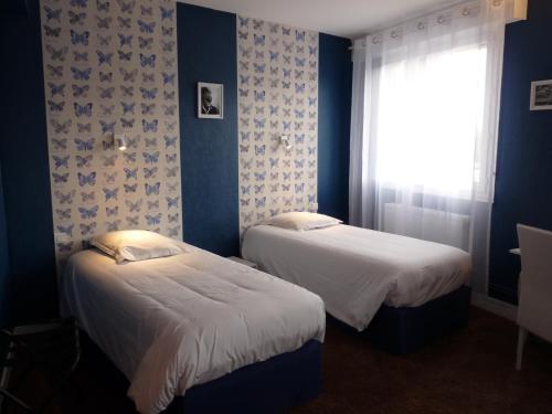 two beds in a room with blue walls and a window at Hôtel Patton in Avranches
