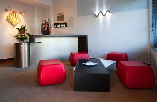 a bar with red chairs and a woman at a counter at Logis Le Relais Saint Jacques in Saint-Léonard-de-Noblat