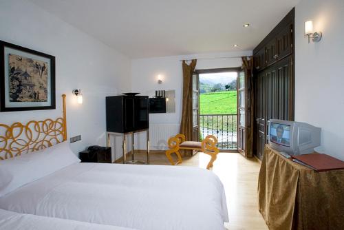 1 dormitorio con cama, TV y balcón en Hotel y apartamentos rurales L'Anceo en Cibuyo