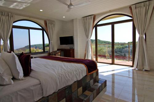 a bedroom with a large bed with large windows at Forest County Resort in Mahabaleshwar