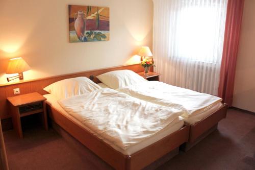Schlafzimmer mit einem Bett mit weißer Bettwäsche und einem Fenster in der Unterkunft Hotel Niederée in Bad Breisig