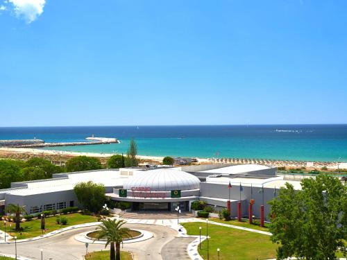 a large white building with a beach in the background at Dom Pedro Portobelo in Vilamoura