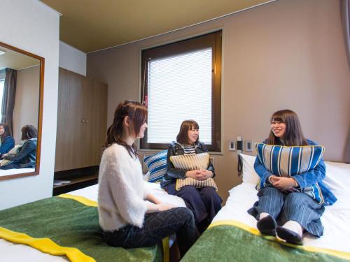 three women sitting on a bed in a room at Hotel AreaOne Nobeoka in Nobeoka