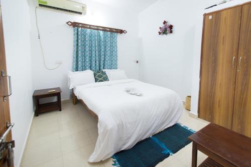 a bedroom with a white bed with a blue curtain at Brittos Homestay in Mandrem