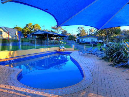 a swimming pool with a blue umbrella and chairs at Beach Cabins Merimbula in Merimbula