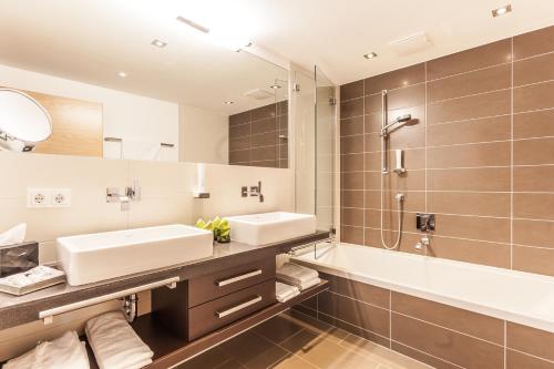 a bathroom with a sink and a tub and a mirror at LEDERER Boutique Hotel in Kaprun