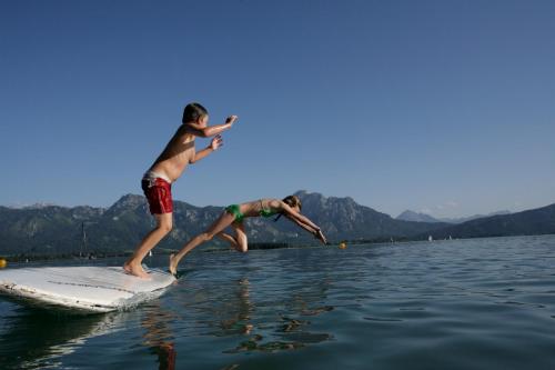 two boys jumping off a surfboard in the water at Cafe Maria - Pension - B&B in Rieden am Forggensee