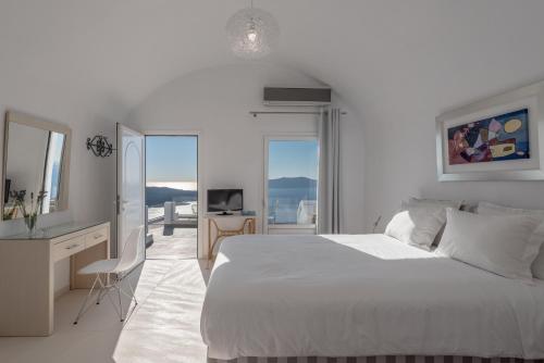 a white bedroom with a bed and a desk and a television at Villa Renos Hotel in Fira