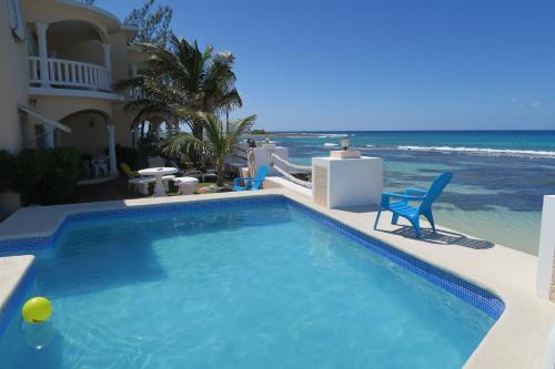 a swimming pool next to a beach with chairs and the ocean at Triplets on the Bay in Montego Bay