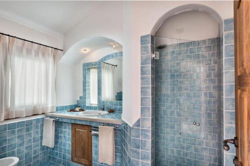 Baño de azulejos azules con lavabo y espejo en Hotel Arathena, en San Pantaleo