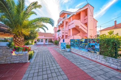 a street in front of a pink building with a palm tree at Villa Dalmatina Zadar mit Pool in Zadar