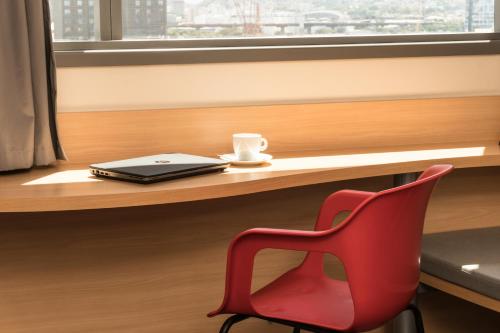 a red chair sitting in front of a desk with a laptop at ibis Rio Porto Atlantico in Rio de Janeiro