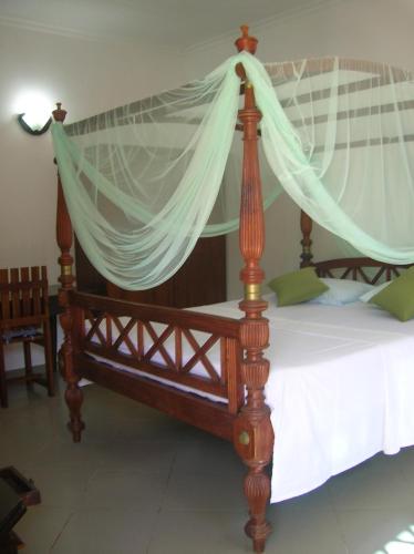 a wooden canopy bed with a white mosquito net at Sagarika Beach Hotel in Moragalla
