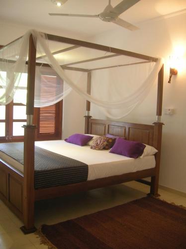 a bedroom with a canopy bed with purple pillows at Sagarika Beach Hotel in Moragalla