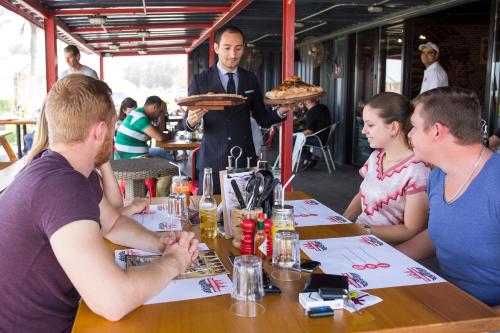 a group of people sitting at a table with a man holding a pizza at Barracuda Resort in Umm Al Quwain