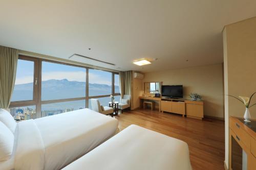 a hotel room with two beds and a large window at Ocean Suites Jeju Hotel in Jeju