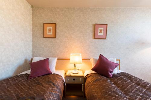 two beds in a hotel room with purple pillows at Sky Hotel Uozu in Uozu