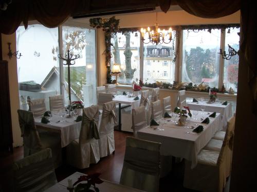 a restaurant with white tables and chairs and windows at Hotel Viktória in Balatonalmádi