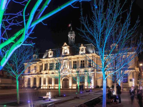 a building lit up at night with trees in front at ibis budget Troyes Est in Saint-Parres-aux-Tertres