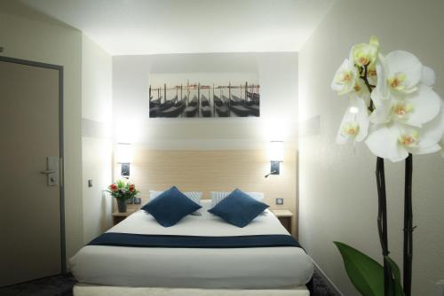 a bedroom with a bed with blue pillows and flowers at Hotel Inn Design Dijon Sud in Marsannay-la-Côte