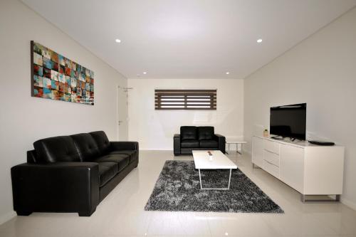 a living room with a black leather couch and a tv at Coastal By Rockingham Apartments in Rockingham