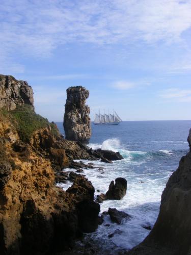a sail boat in the ocean next to a rocky coast at Peniche Hostel in Peniche