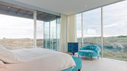 a bedroom with a bed and a chair and glass windows at Bahia Vik in José Ignacio