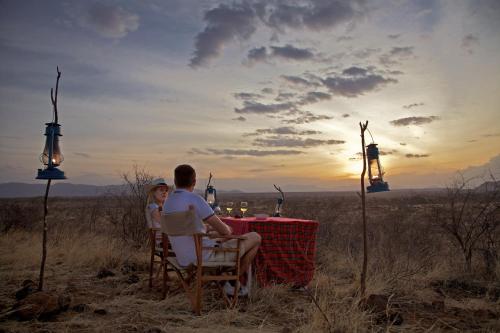 a man and a woman sitting at a table with the sunset at Ashnil Samburu Camp in Archers Post
