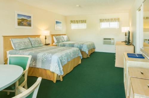 two beds in a room with a table and a kitchen at Surfcomber On The Ocean in South Yarmouth