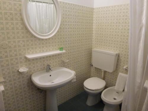 Un baño con lavabo, inodoro y espejo. en Hotel San Marco, en Lignano Sabbiadoro