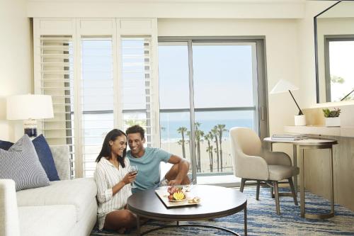 a man and a woman sitting at a table in a living room at Loews Santa Monica Beach Hotel in Los Angeles