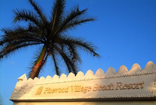 a palm tree behind a sign for a beach resort at Pinewood Beach Resort and Spa in Diani Beach
