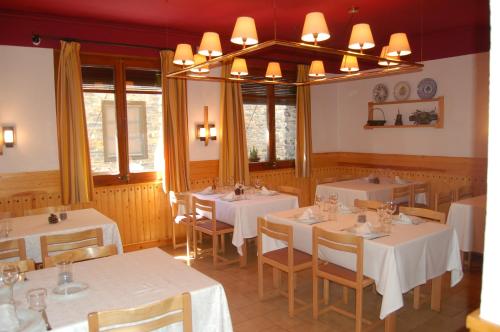 un restaurante con mesas y sillas blancas y ventanas en Hotel Vall Ferrera, en Àreu