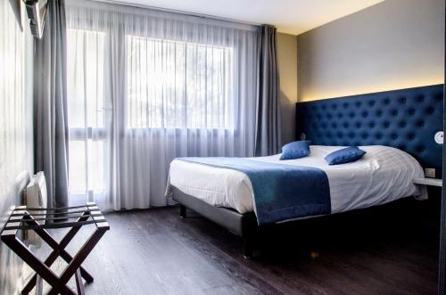 une chambre avec un grand lit et une tête de lit bleue dans l'établissement The Originals City, Hôtel Les Caps, Saint-Brieuc Est, à Lamballe