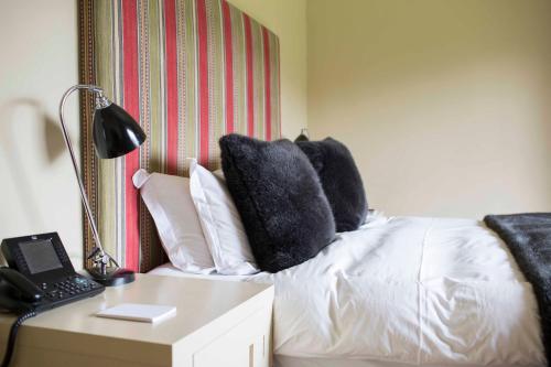 a bed with black pillows and a table with a lamp at Milsoms Kesgrave Hall in Ipswich