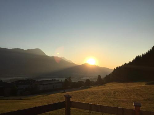 a sunset over a field with the sun setting on a mountain at Appartement Hauser Kaibling in Haus im Ennstal